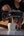 A person pours coffee from a glass carafe into a ceramic mug next to a bag of Cinco Cielos coffee, set against a dark background.