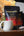 A bag of Cinco Cielos Coffee beans in front of a white ceramic mug on a wooden surface, with a coffee maker blurred in the background.